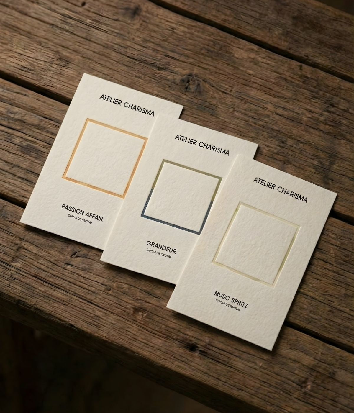 Three ivory Olfactory Library scent cards for Passion Affair, Grandeur and Musc Spritz on a wooden table